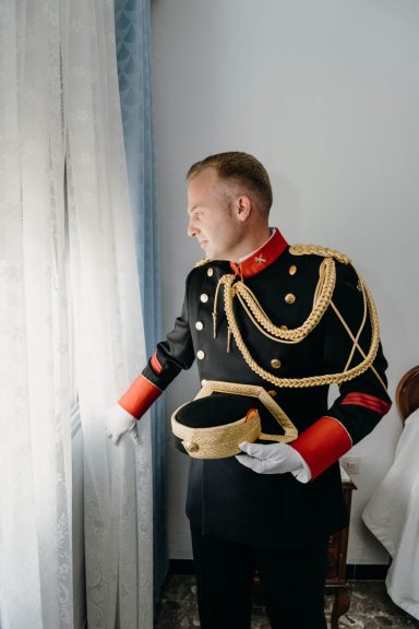 Hombre con uniforme militar, mirando por la ventana y sosteniendo un sombrero.