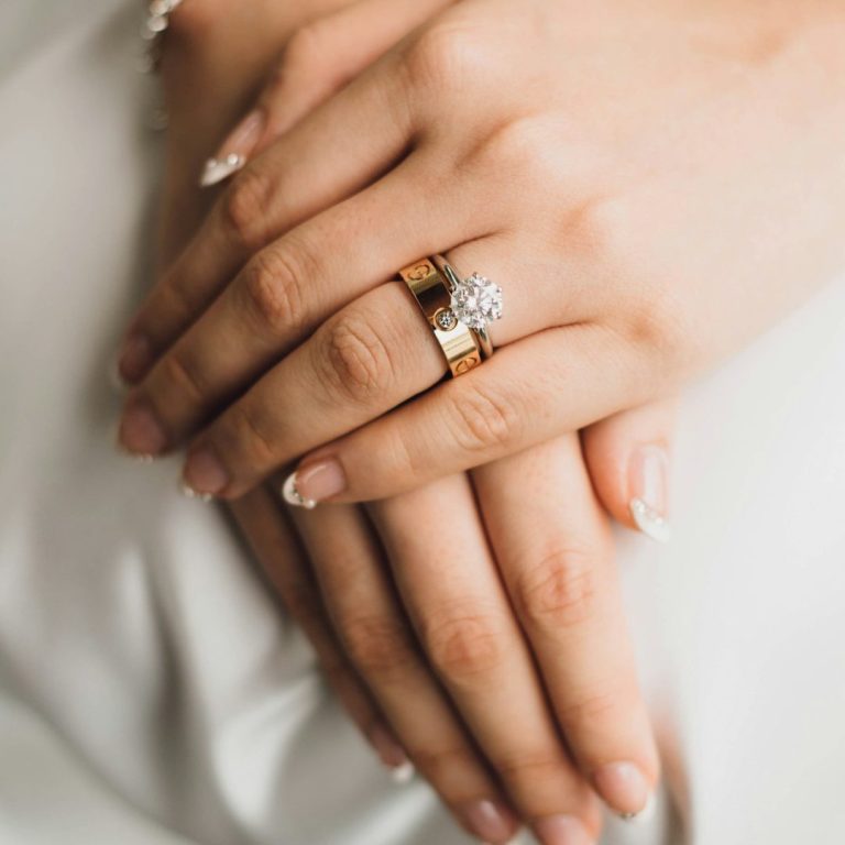 Manos entrelazadas con anillos de matrimonio y compromiso, uñas decoradas.